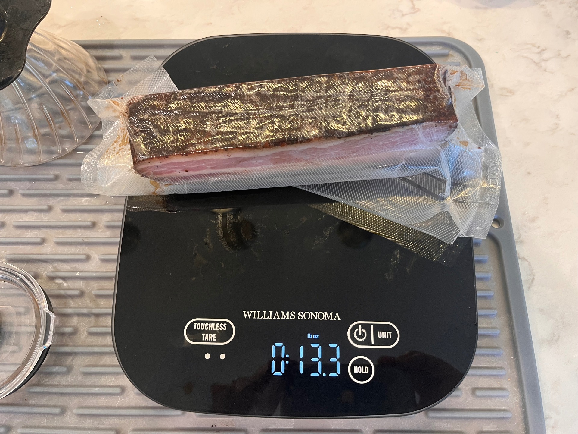 Vacuum-sealed portion of smoked bacon on a kitchen scale reading 13.3 ounces