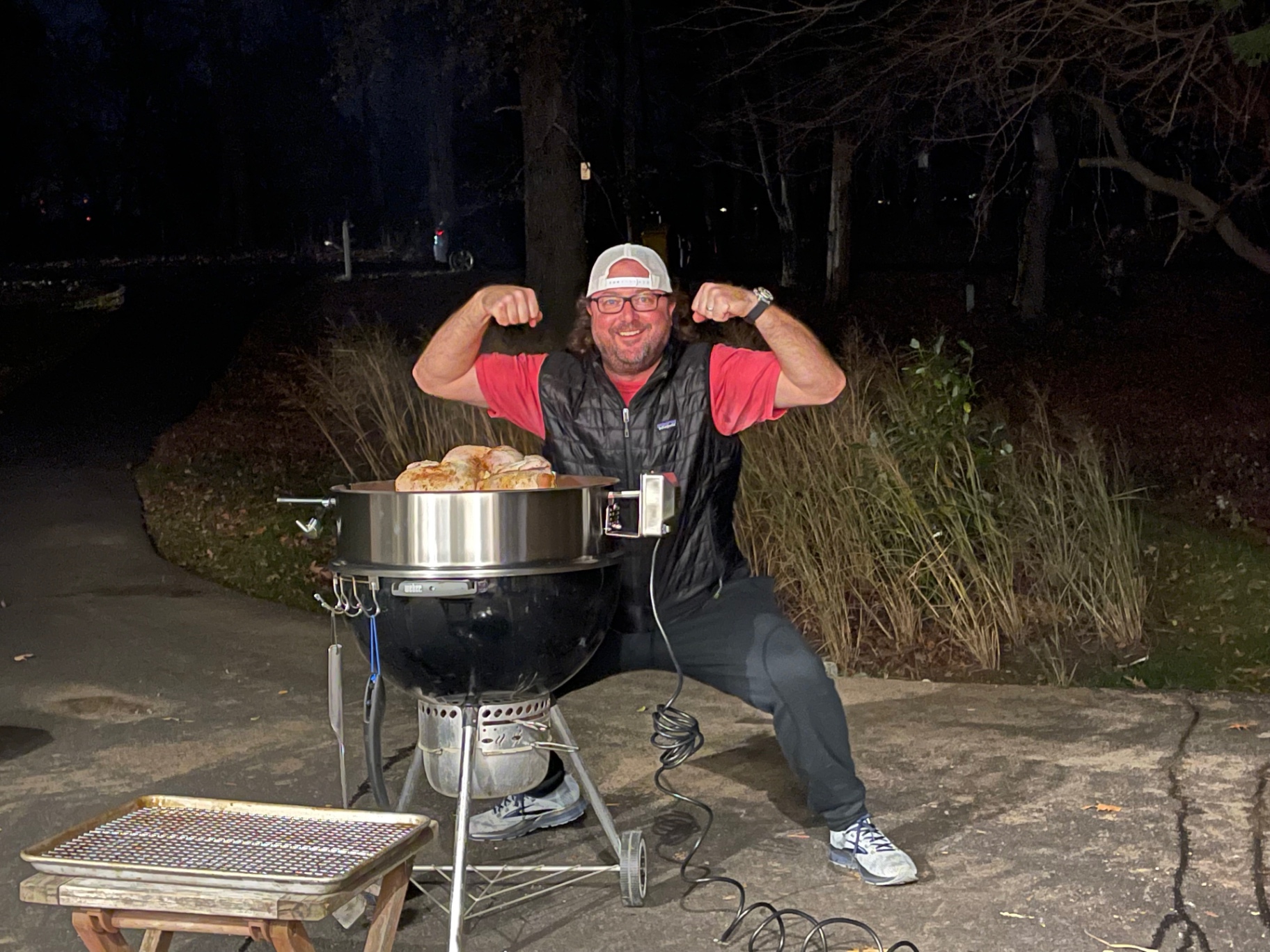 A cook celebrating beside a charcoal rotisserie at night