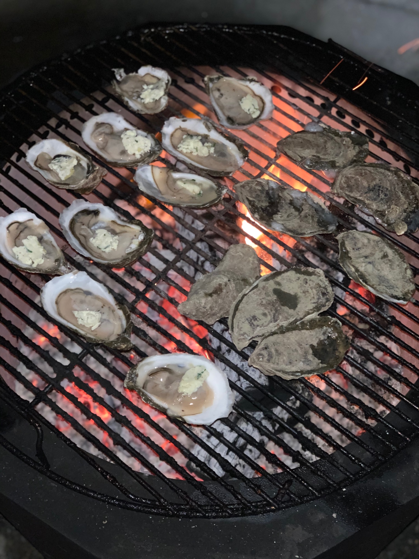 Oysters topped with butter and herbs over glowing coals