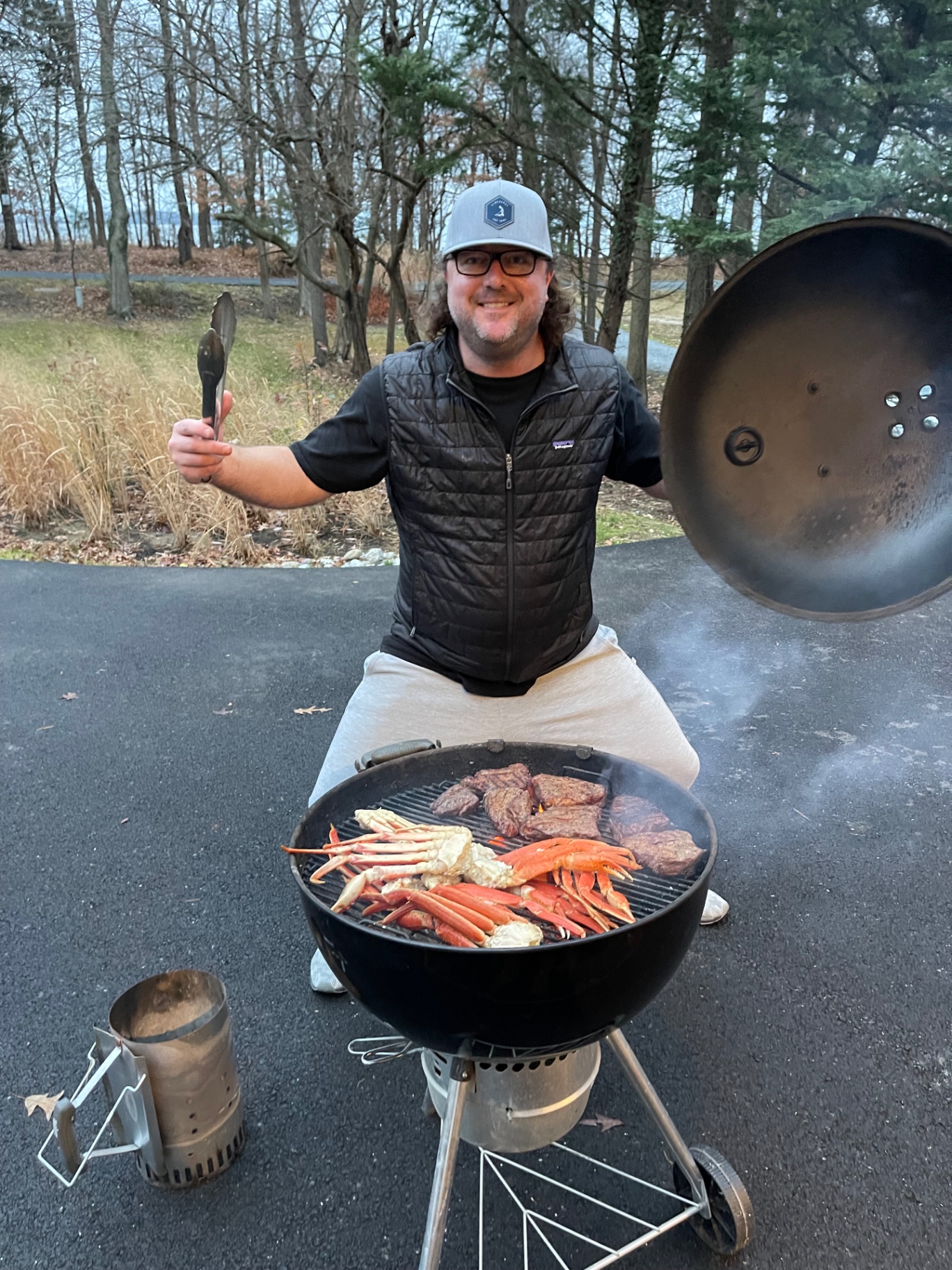 A cook posing behind a grill full of steaks and crab legs