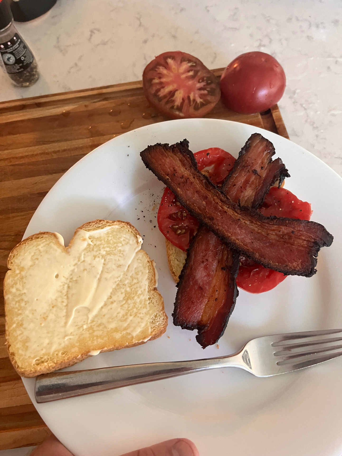 Thick-cut home-cured bacon on sliced garden tomatoes beside a slice of mayo-spread toast