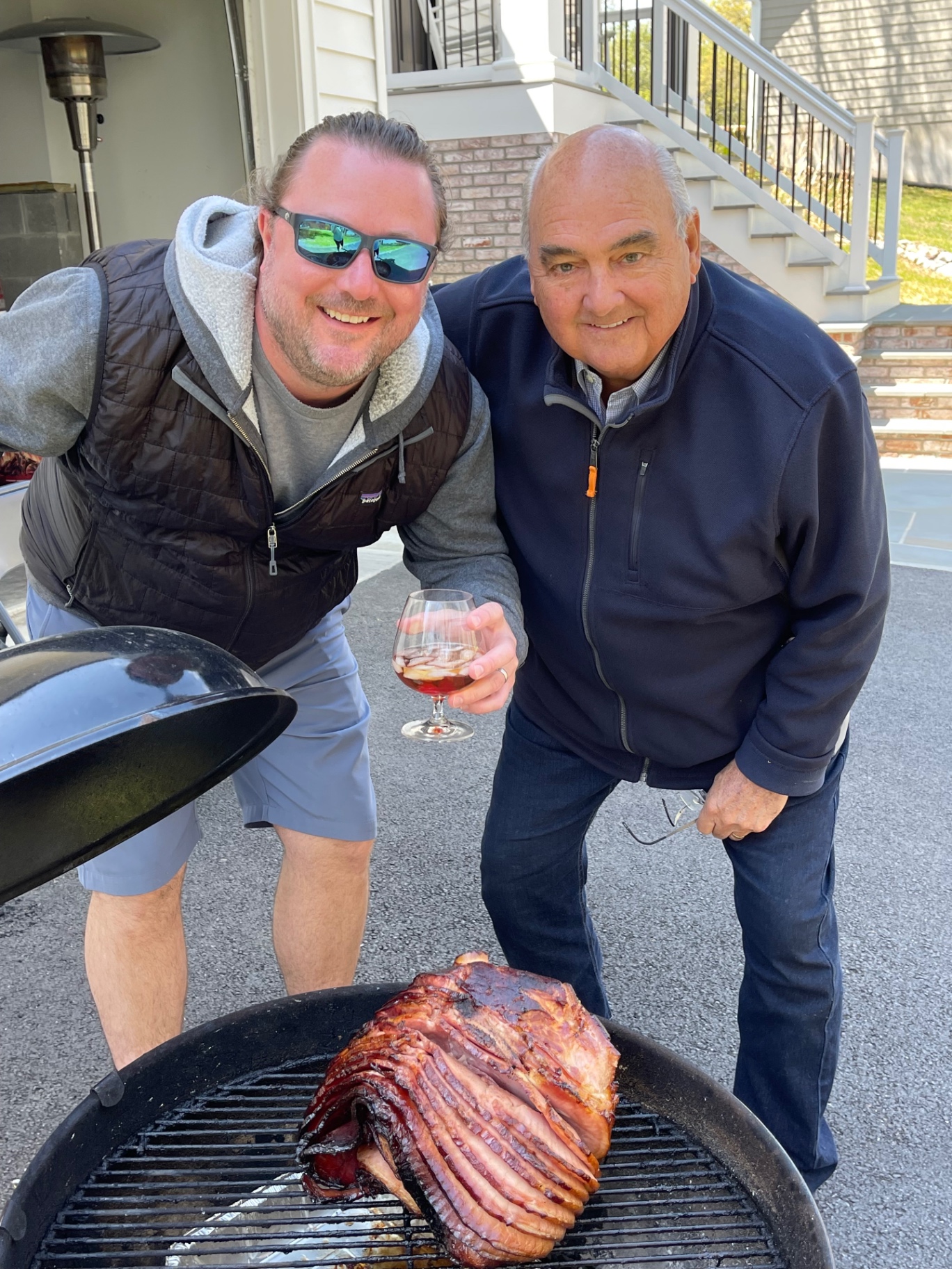 Two generations smiling over a glazed spiral ham on the grill