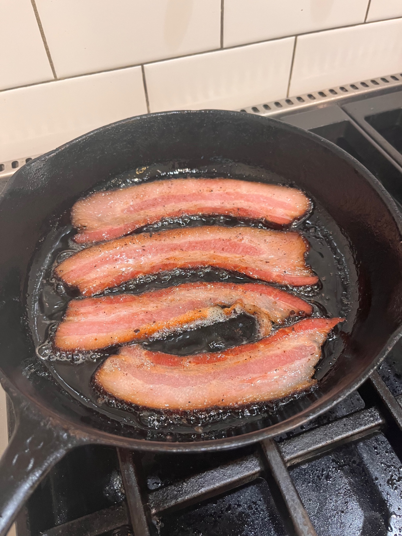 Thick-cut bacon slices crisping and bubbling in a cast iron skillet