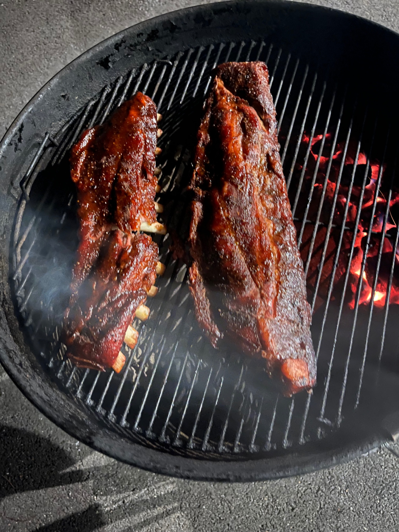 Two racks of glazed ribs smoking over glowing charcoal at night