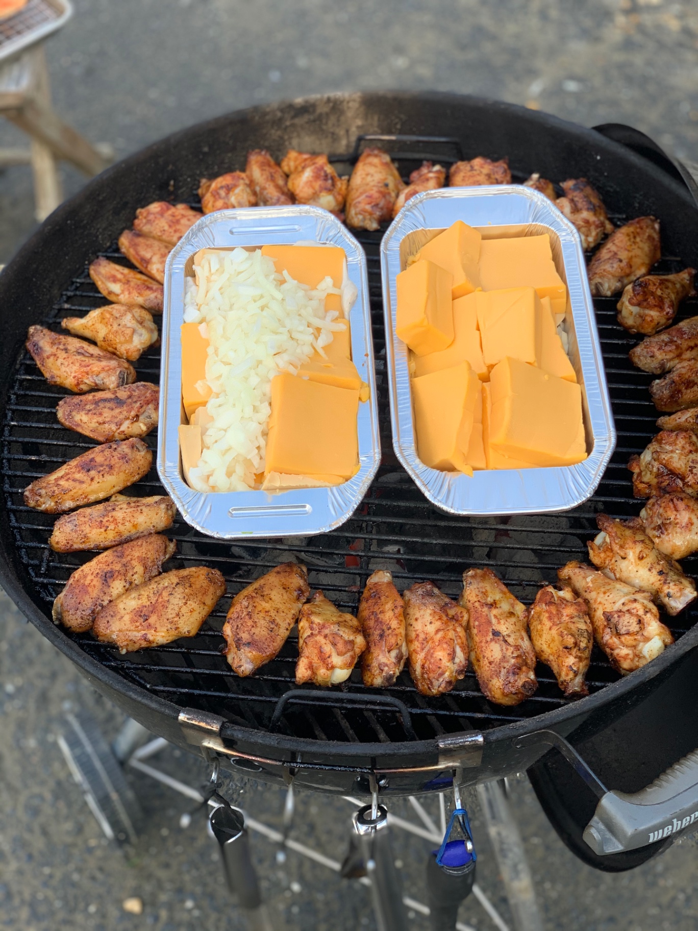 Chicken wings surrounding pans of cheese and onion on a kettle grill