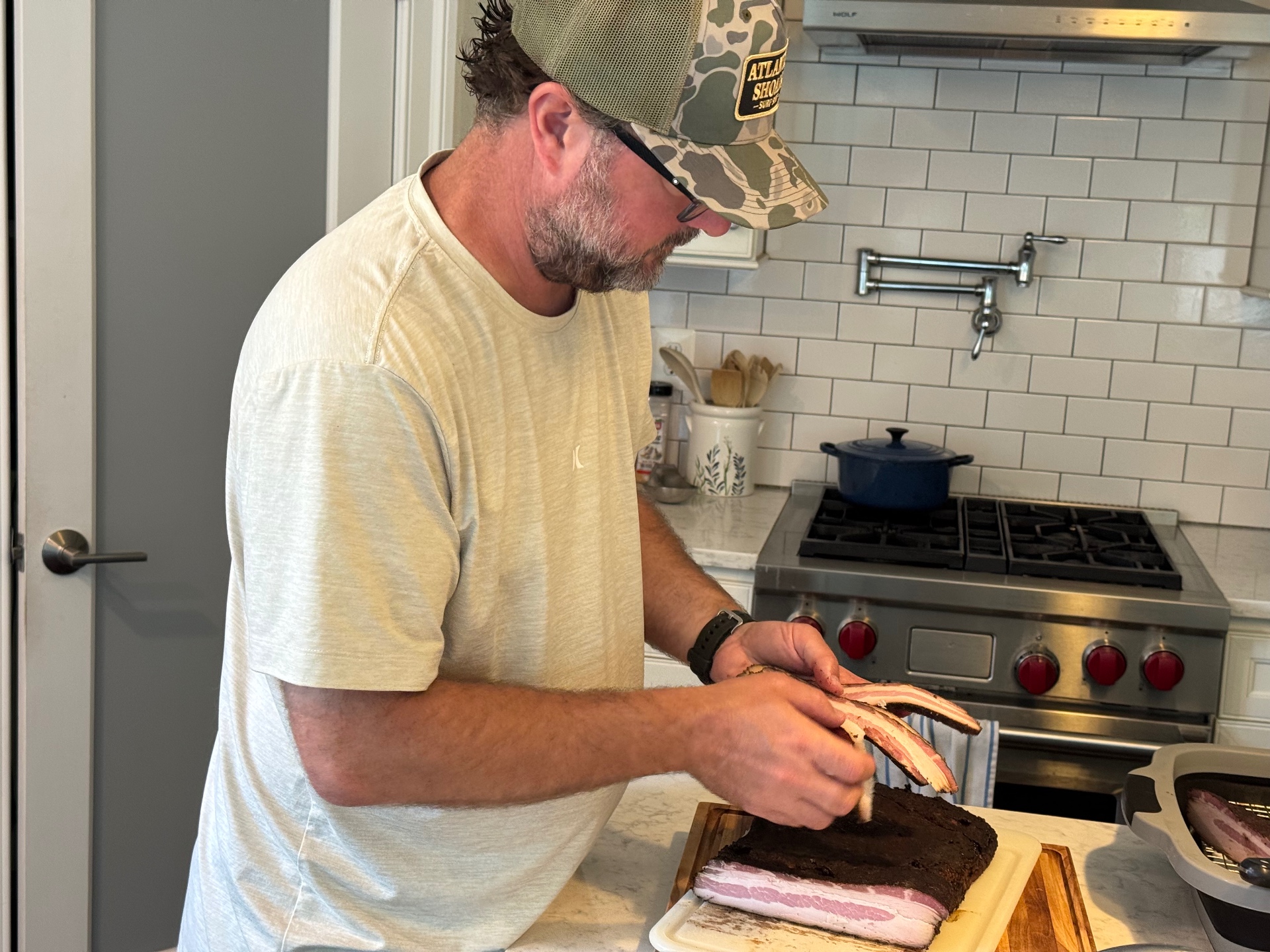 Hand slicing the chilled, smoked bacon slab on a cutting board