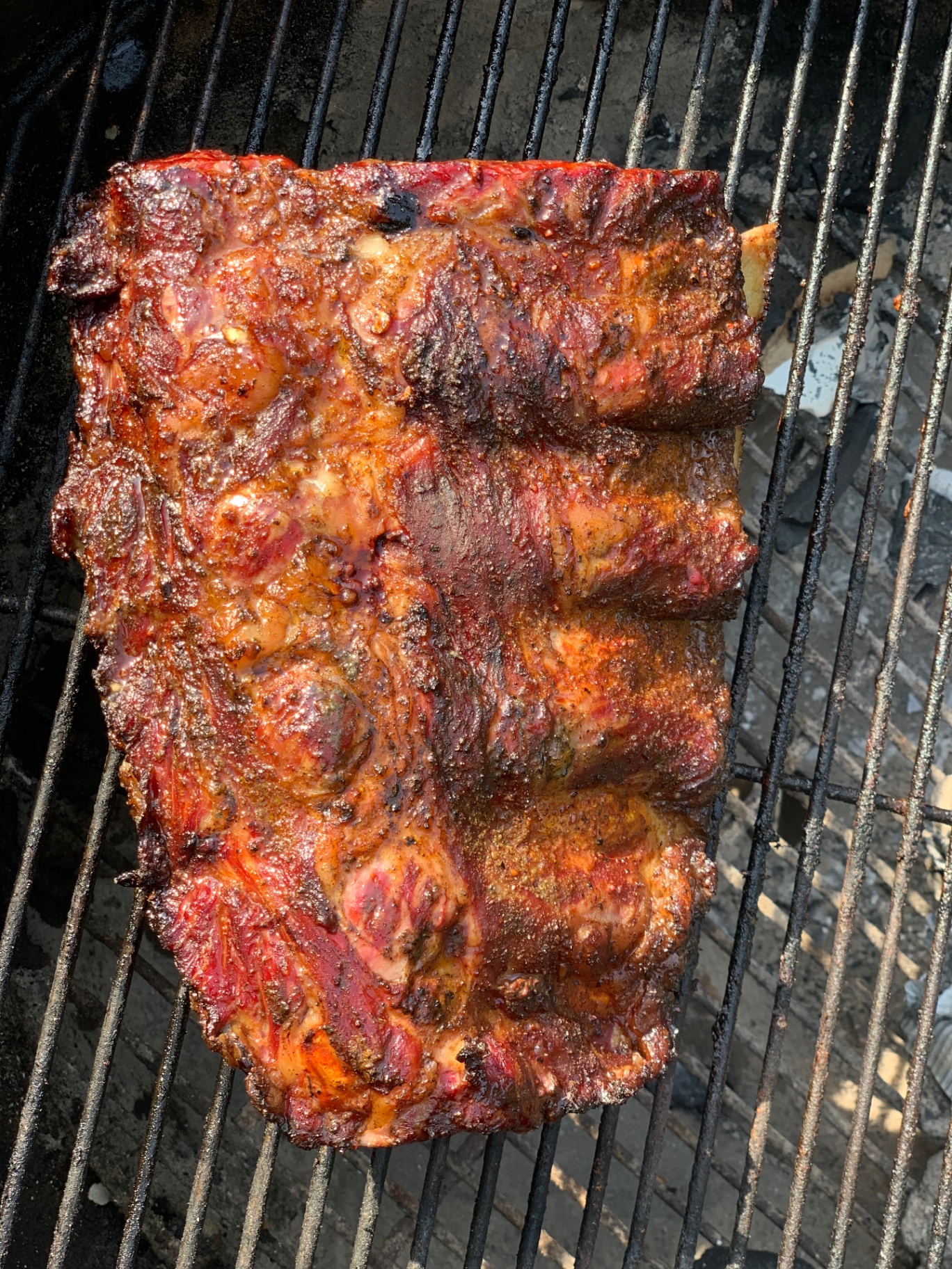 A dark-rubbed slab of ribs cooking on the grill