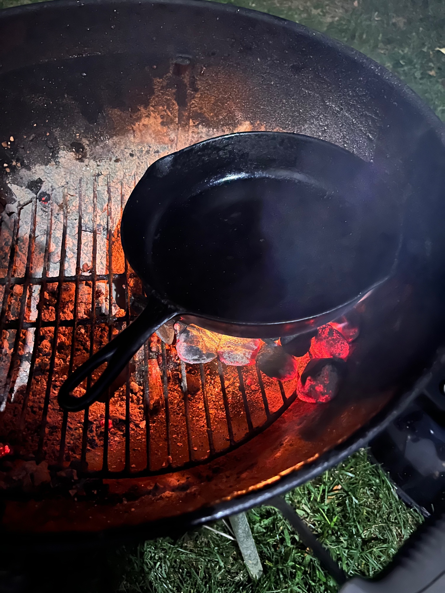Cast iron skillet set directly over glowing charcoal inside the kettle