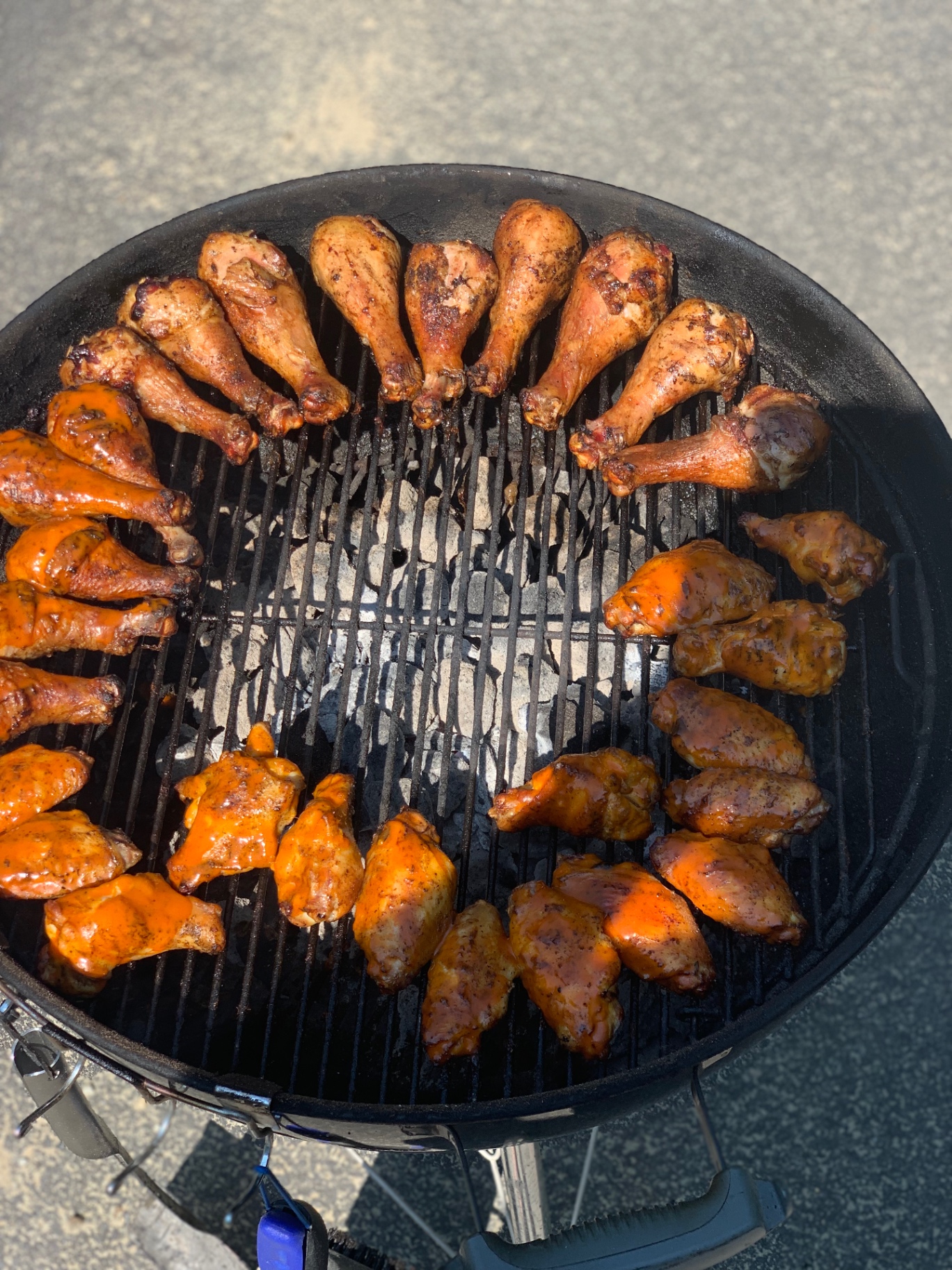 Drumsticks and wings arranged in a ring on a charcoal grill
