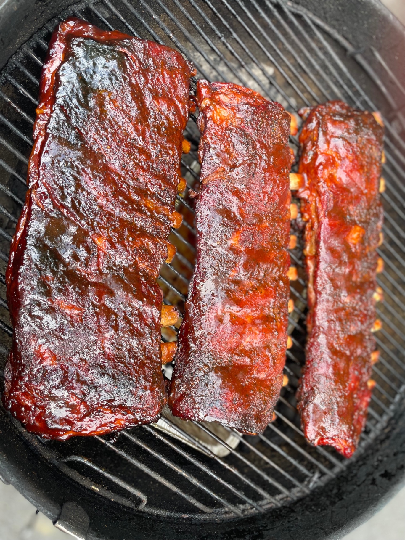 Three glossy racks of ribs finishing on a charcoal grill