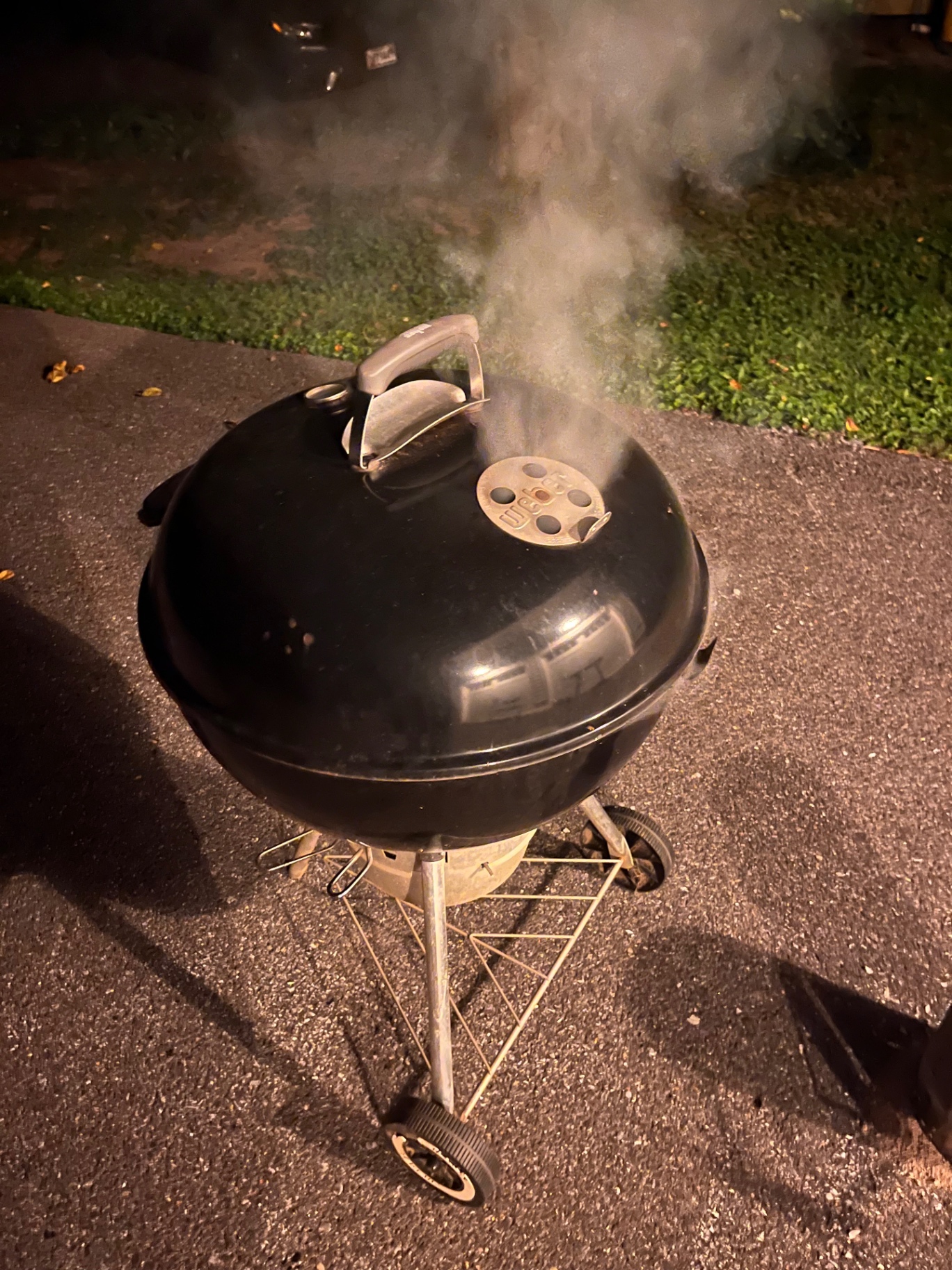 Weber kettle grill smoking at night on a driveway