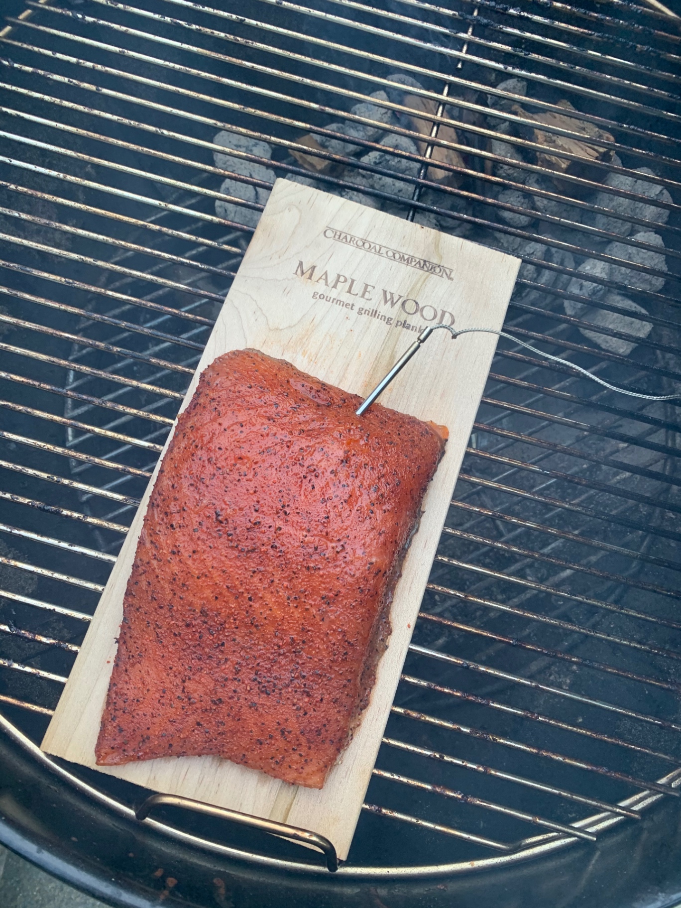 Seasoned salmon cooking on a maple plank over charcoal