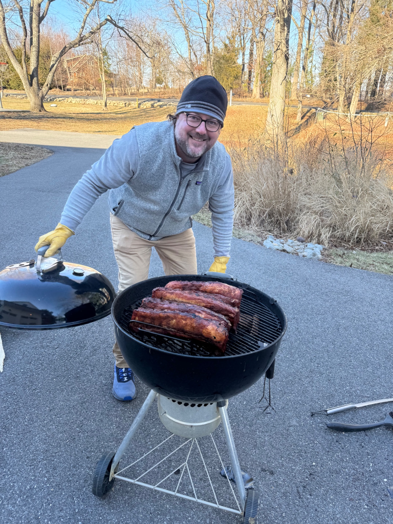 A cook showing several racks of ribs on a charcoal grill