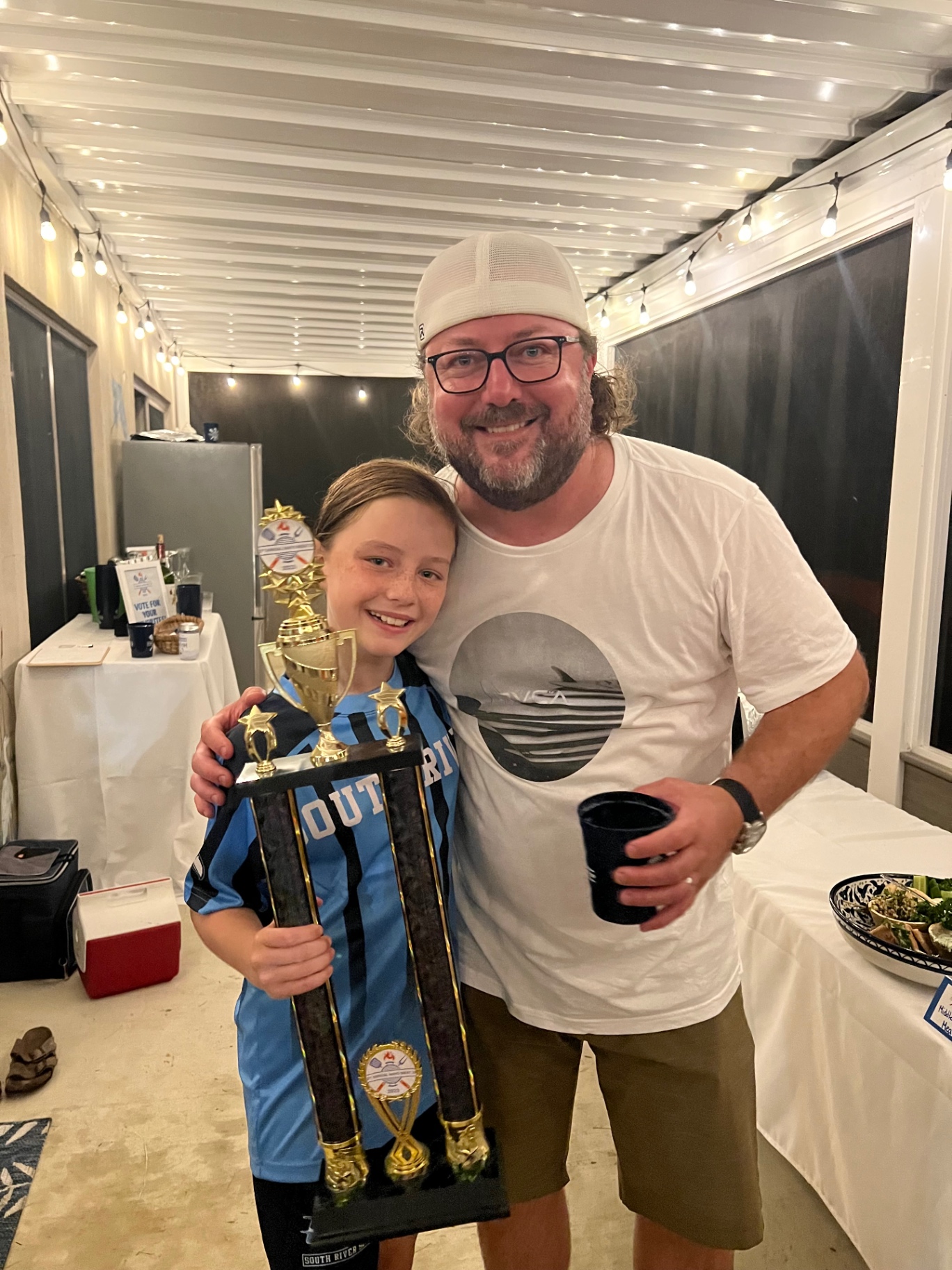 A proud father and daughter holding a large soccer trophy